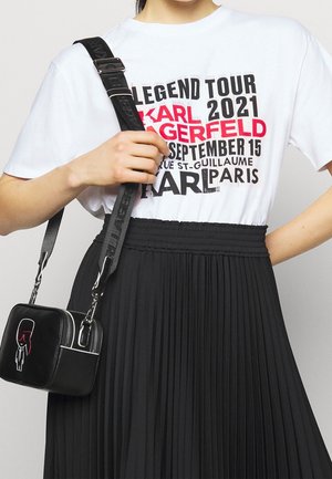 T-shirt blanc avec texte audacieux en noir et rouge, associé à une jupe plissée noire. Sac à main noir avec un design graphique et des garnitures en argent.