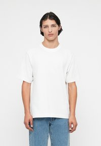 Valge lühikeste varrukatega puuvillane T-särk, millel on ümar kaelus ja mugav lõige. Koos helesiniste teksapükstega.