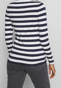 Marinblå och vit randig långärmad topp i ett stretchigt material, med rundad halsringning och något böjd sidsöm. I kombination med mörkgrå jeans.