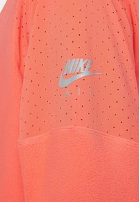 Sudadera de Nike con tejido coral transpirable, textura perforada, panel inferior de felpa y un logo de Nike Air en plateado.
