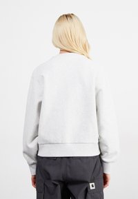 Jasnoszara bluza z okrągłym dekoltem, ściągaczami przy mankietach i u dołu. Miękka faktura, prosty design i brak widocznych logo lub wzorów.