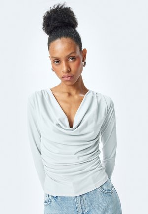 Lichtblauw coltrui met lange mouwen, met een geplooide structuur langs de torso. Glad stof met een slim fit.
