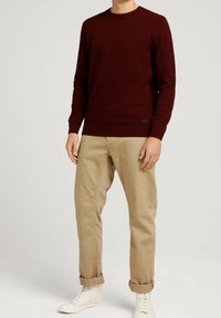 Bordowy sweter dzianinowy z fakturowanym wzorem, okrągłym dekoltem, ściągaczami na rękawach i dole, w połączeniu z jasnobeżowymi, podwiniętymi chinosami oraz białymi tenisówkami.