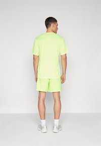 Neon-grünes Sportset mit einem kurzärmeligen Oberteil und Shorts, aus leichtem, glattem Material. Enthält sichtbare Nähte und einen Rundhalsausschnitt.