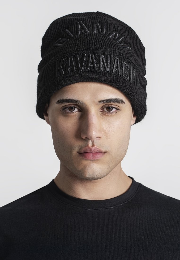 Cappello di lana nera lavorato a maglia con lettering in rilievo "GIANNA KAVANAGH". Indossato da una persona con una maglietta nera, presenta un design adesivo e un tessuto testurizzato.