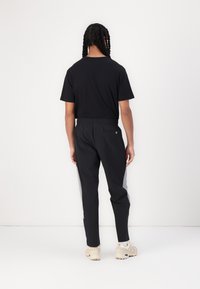 Sort t-shirt med korte ærmer, parret med sorte bukser med grå sidelister og elastisk talje. Casual fodtøj.