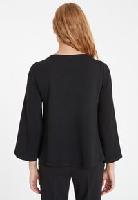 Schwarzes Langarmoberteil mit Rundhalsausschnitt und locker fallenden, glockenförmigen Ärmeln. Glatte Textur und schlichtes Design, geeignet zum Layering.