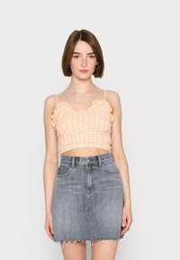 Top cropped laranja e branco com estampado quadriculado e bordas com babados, combinado com uma saia de ganga cinza de cintura alta com bainha desfiada e bolsos frontais.