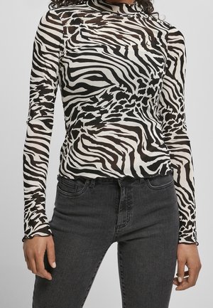 Langärmliges Oberteil aus durchsichtiger Stoff mit einem schwarz-weißen Zebra-Muster, mit hohem Ausschnitt und taillierter Passform. Kombiniert mit schwarzen Jeans.
