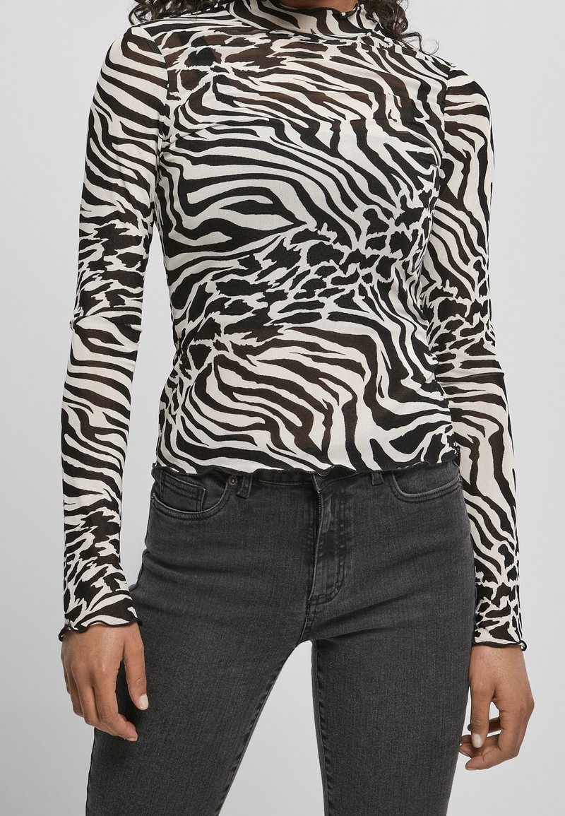Långärmad topp i genomskinligt tyg med svart och vitt zebramönster, med hög halsringning och figurnära design. Matchad med svarta jeans.