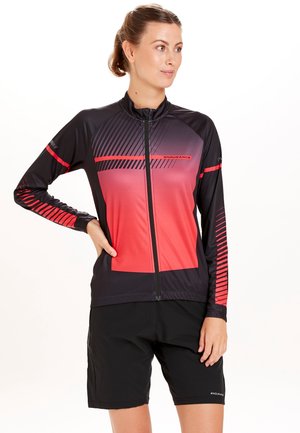 Veste de sport noire et rouge avec fermeture éclair intégrale, présentant un design dégradé et des accents rayés. Portée avec un short noir, fabriqué en tissu à séchage rapide.