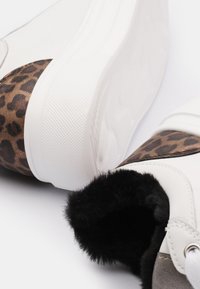 White faux leather sneakers with a brown leopard print accent, textured sole, and black fur lining around the ankle. Rubber sole.