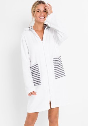 Accappatoio bianco con cappuccio realizzato in morbido tessuto testurizzato, dotato di zip frontale e tasche a righe grigie e bianche.