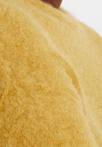 Suéter de lana amarillo con una textura suave y esponjosa, y un corte relajado. Presenta un escote redondo y detalles de costura sutiles.