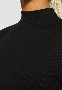 Maglione a collo alto nero con coste, caratterizzato da un collo alto, una texture sottile, un design aderente e una costruzione senza cuciture per un aspetto pulito.