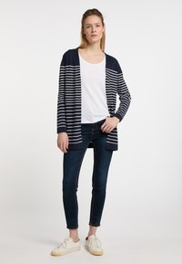 Cardigan aperto a righe blu navy e bianche, con maniche lunghe e tessuto leggero. Abbinato a una maglietta bianca e jeans scuri.