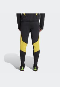 Schwarze Leggings mit gelben, winkeligen Akzenten, strukturierten Einsätzen und einer enganliegenden Passform, mit einem Logo an den Seiten und Performance-Schuhwerk.