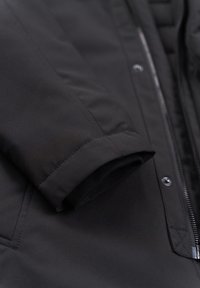 Schwarze Jacke mit glatter Textur, Reißverschluss und elastischen Bündchen. Auffällige Nähte und ein gepolstertes Innenfutter für Isolierung.