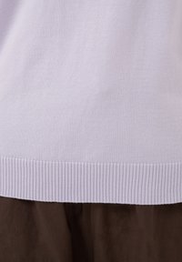 Ourlet de pull en maille violet clair sur tissu marron foncé, montrant la texture et le motif côtelé en bas du pull.