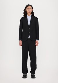 Schwarze Sakko mit zwei Knöpfen, passende schwarze Hose und ein hellblaues Hemd. Texturiertes Material, taillierte Passform und glatte Oberfläche.