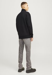 Sudadera negra de cuello alto combinada con jeans de mezclilla grises. Tela suave y ajuste relajado. Los zapatos son negros con una ligera plataforma.