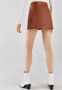 Hnědá kožená mini sukně s rovnými liniemi a texturovaným povrchem, s vysokým pasem a jemnými švy, v kombinaci s bílými kotníkovými botami.