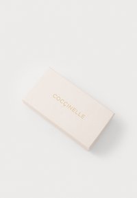 Coccinelle márkáj�ú, világos rózsaszín doboz, sima textúrával. Az tetején egyszerű arany felirat található. Téglalap alakú, minimalista dizájn.