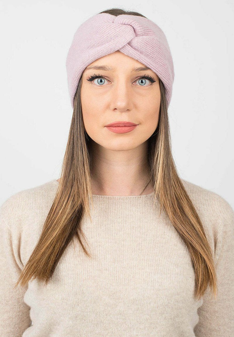 Fascia in maglia rosa con design intrecciato, texture morbida e vestibilità aderente. Indossata da una persona con capelli lunghi e un maglione beige chiaro.