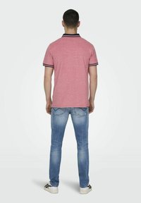 Rood heather polo shirt met navy kraag en mouwaccenten, gecombineerd met lichtblauwe jeans en witte sneakers, bekeken vanaf de achterkant.