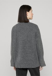 Pull gris oversize avec une texture tricotée, manches larges et un ourlet légèrement effiloché, vu de dos.