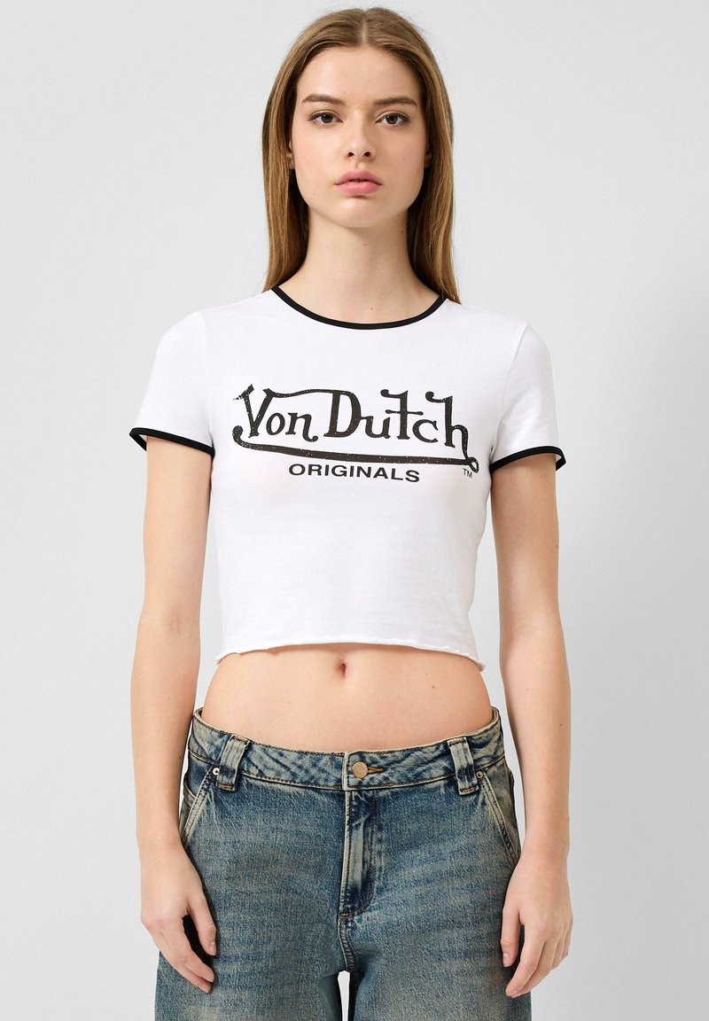 Weißes, kurzes T-Shirt mit schwarzem geripptem Ausschnitt und Ärmelabschlüssen. Mit einem Frontdruck: "Von Dutch ORIGINALS" in fetter schwarzer Schrift.