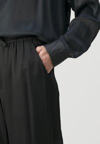 Svart, slätt tygskjorta med avslappnad passform och långa ärmar, tillsammans med svarta byxor med elastisk midja och sidfickor.