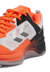 Jasnopomarańczowy but sportowy z siateczkową cholewką, czarnymi akcentami, białymi detalami i teksturowaną podeszwą. Posiada wyraźne logo oraz mocny system sznurowania.