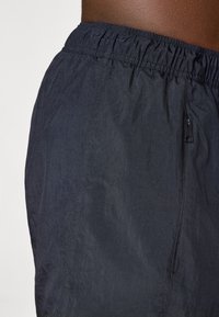 Sort vævede shorts med elastisk talje, der har en sidelomme med lynlås, glat tekstur og et let design.