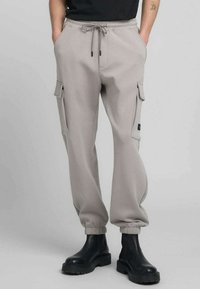Pantaloni cargo grigio chiaro con polsini elasticizzati, vita con coulisse e tasche laterali. Realizzati in tessuto morbido con una consistenza liscia.