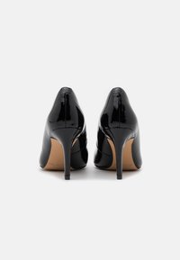Escarpins en cuir verni noir avec un bout pointu et un talon aiguille cranté. Fini lisse, design minimaliste et semelle intérieure visible.