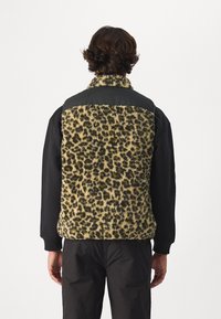 Fleece vest so vzorom leopardích škvrn s čiernymi nylonovými detailami, vysokým golierom, zipsom a voľným strihom; textúrovaný povrch s rôznymi odtieňmi žltej a čiernej.