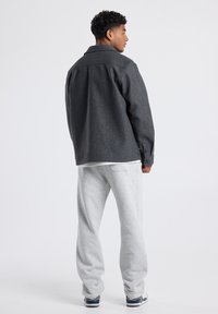 Gray wool blend jacket with large collar and button fastening, paired with light gray sweatpants and casual sneakers. Simple, relaxed fit.