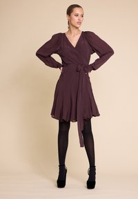 Kjole i dyp burgunder, laget av lett stoff. Har lange pufferm, en knytning i midjen og en utsvingt skjørt. Brukt med svarte strømpebukser og hæler.