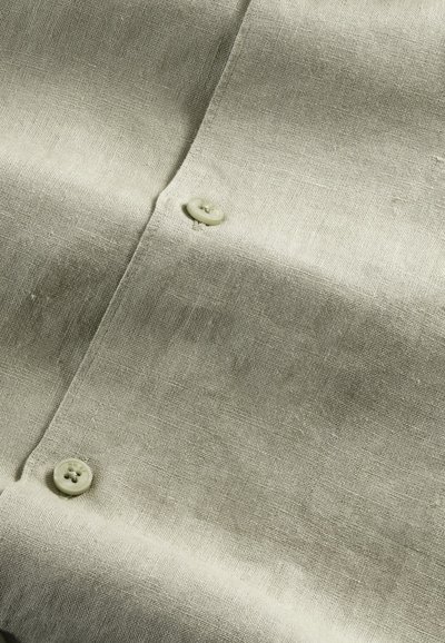 Lys grøn linen skjorte med en glat tekstur, der har to store knapper og et subtilt vævemønster.