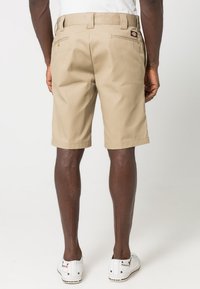 Beiga bomullsshorts med rak skärning, bältesömmar och två bakfickor. Bärs med vita sneakers och en enkel vit skjorta.