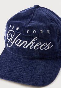 Navy blue cotton cap featuring white embroidered text "NEW YORK Yankees," with a curved brim and textured fabric surface.