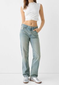 Ljusblå denimjeans med rak ben design, hög midja och subtila blekningsdetaljer. Matchas med en vit croppad topp och silverfärgade sneakers.