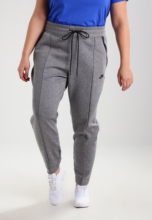Person iført grå Nike sweatpants med sort snøre og lynlåslomme, kombineret med hvide sneakers og en blå skjorte.
