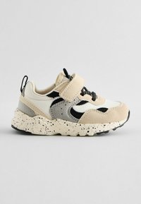 Sneaker multicolore avec des panneaux blancs, beiges et noirs, des matériaux texturés, une semelle mouchetée, une bande Velcro, et une poignée à l'arrière.