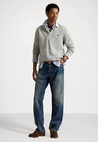 Γκρι μακρυμάνικο πουλόβερ με γιακά, φορεμένο πάνω από ένα μπλε καρό πουκάμισο, συνδυασμένο με ξεθωριασμένο μπλε τζιν και καφέ παπούτσια με κορδόνια.