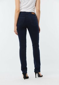 Jeans bleu foncé au style ajusté, taille mi-haute, et deux poches arrière. Fabriqués en tissu denim avec une texture lisse.