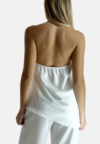 Top in satin bianco presenta un corpetto aderente con schiena arricciata e orlo fluido, abbinato a pantaloni larghi coordinati.
