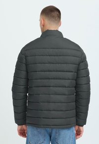 Melnā pūkains jaka ar horizontālu quilted dizainu, ar augstu apkakli un elastīgām aprocēm, izgatavota no gludas, ūdensizturīgas materiāla.