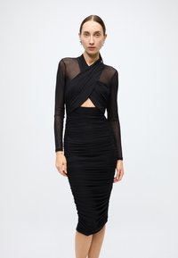 Black ruched dress with sheer long sleeves, featuring a wrapped bodice and a cut-out detail at the midsection for a fitted silhouette.